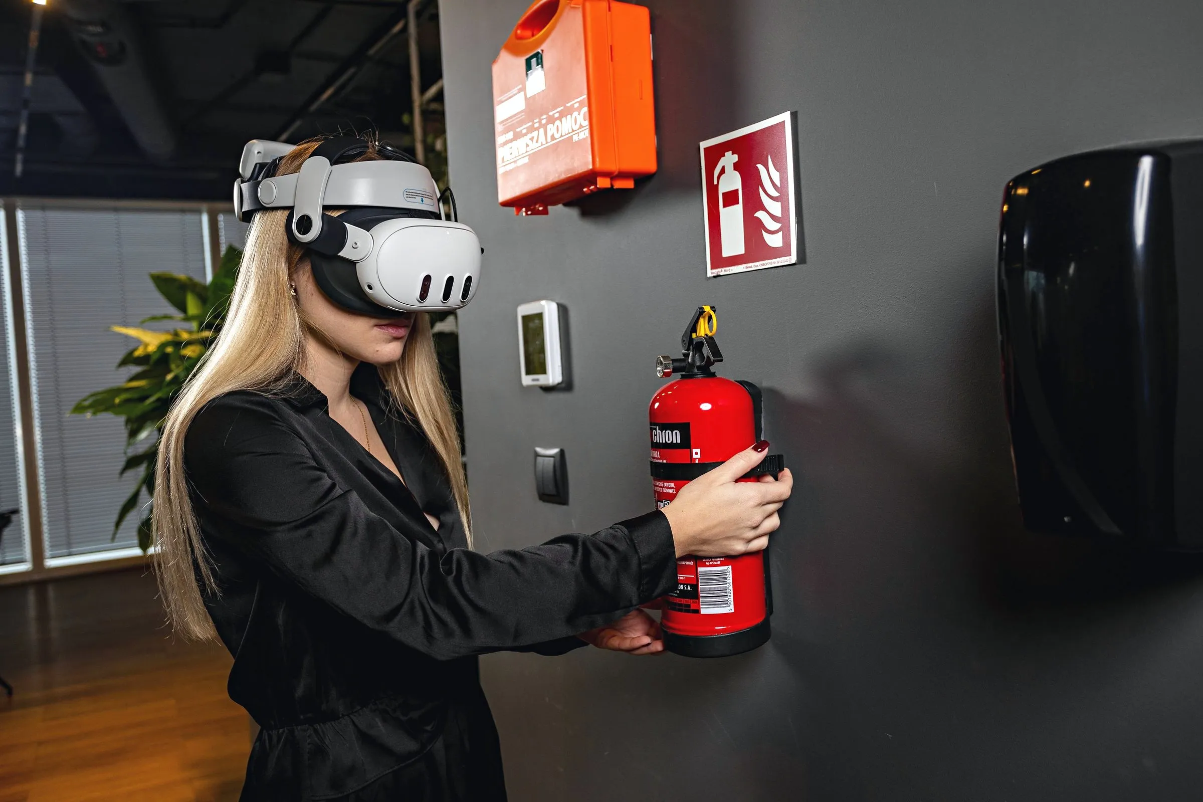 Eine Frau mit VR-Brille greift nach einem Feuerlöscher an der Wand