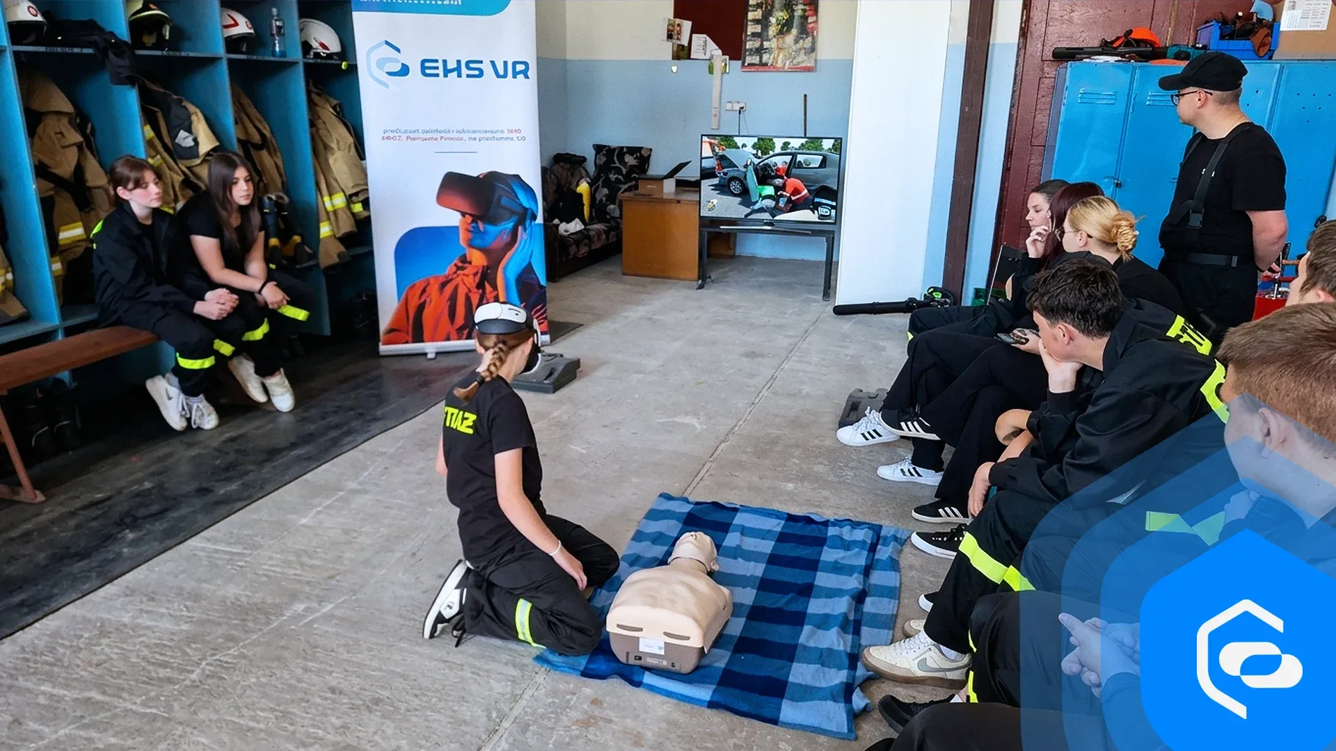 A girl in a VR headset practises resuscitation on a manikin while young volunteer firefighters watch in a fire station