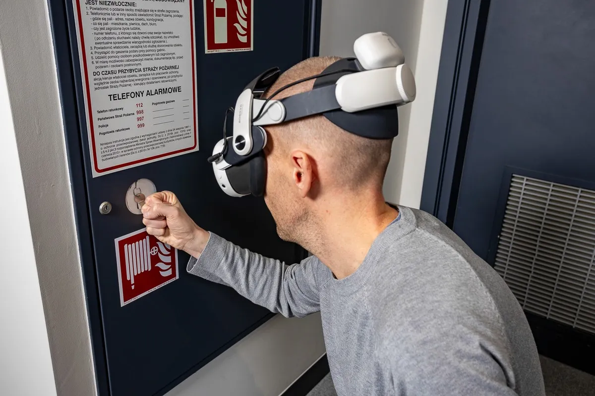 Uczestnik w goglach VR przy tablicy z instrukcją przeciwpożarową