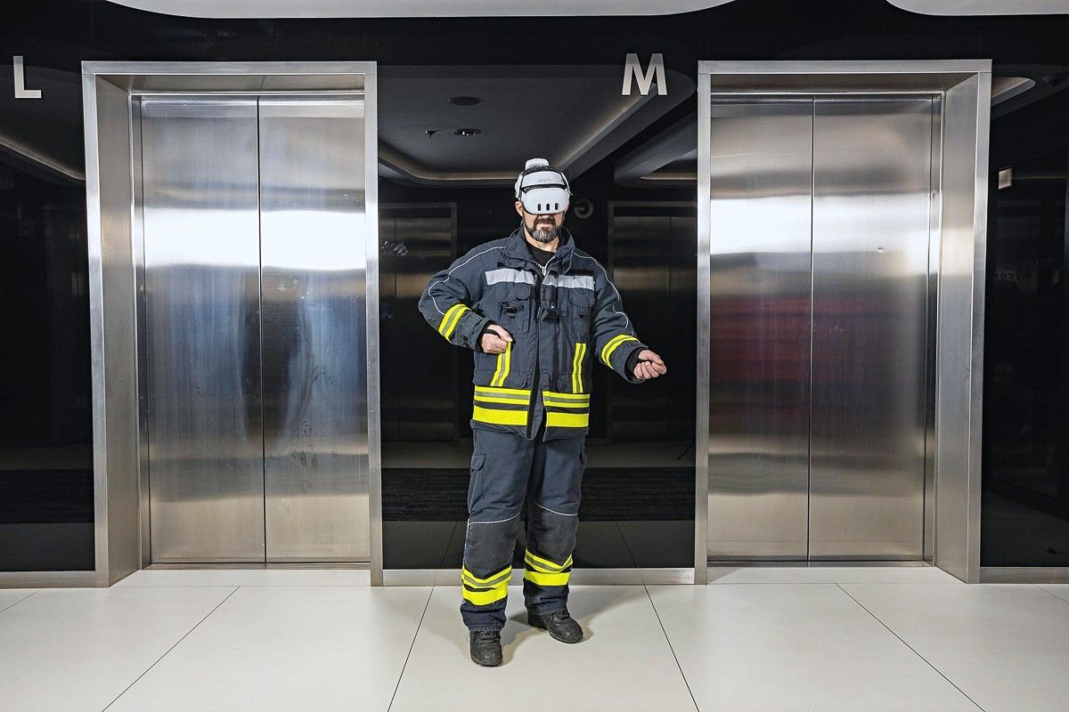 A firefighter by the elevators, wearing a VR headset and holding a virtual fire extinguisher