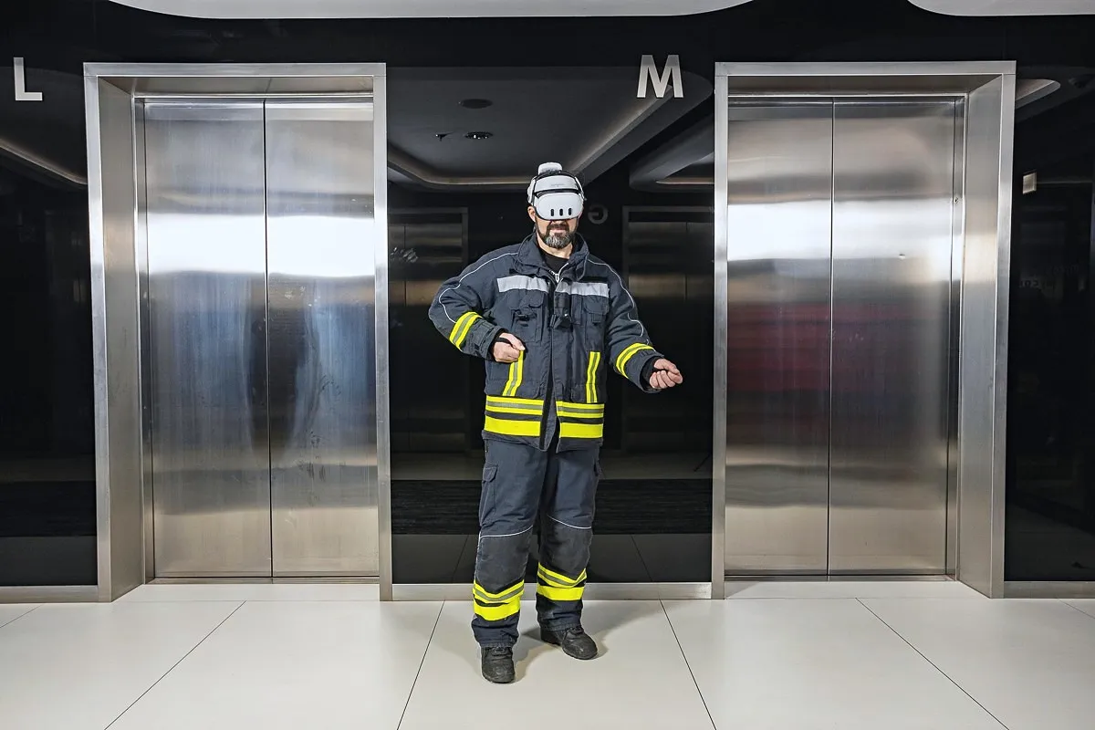 A firefighter by the elevators, wearing a VR headset and holding a virtual fire extinguisher