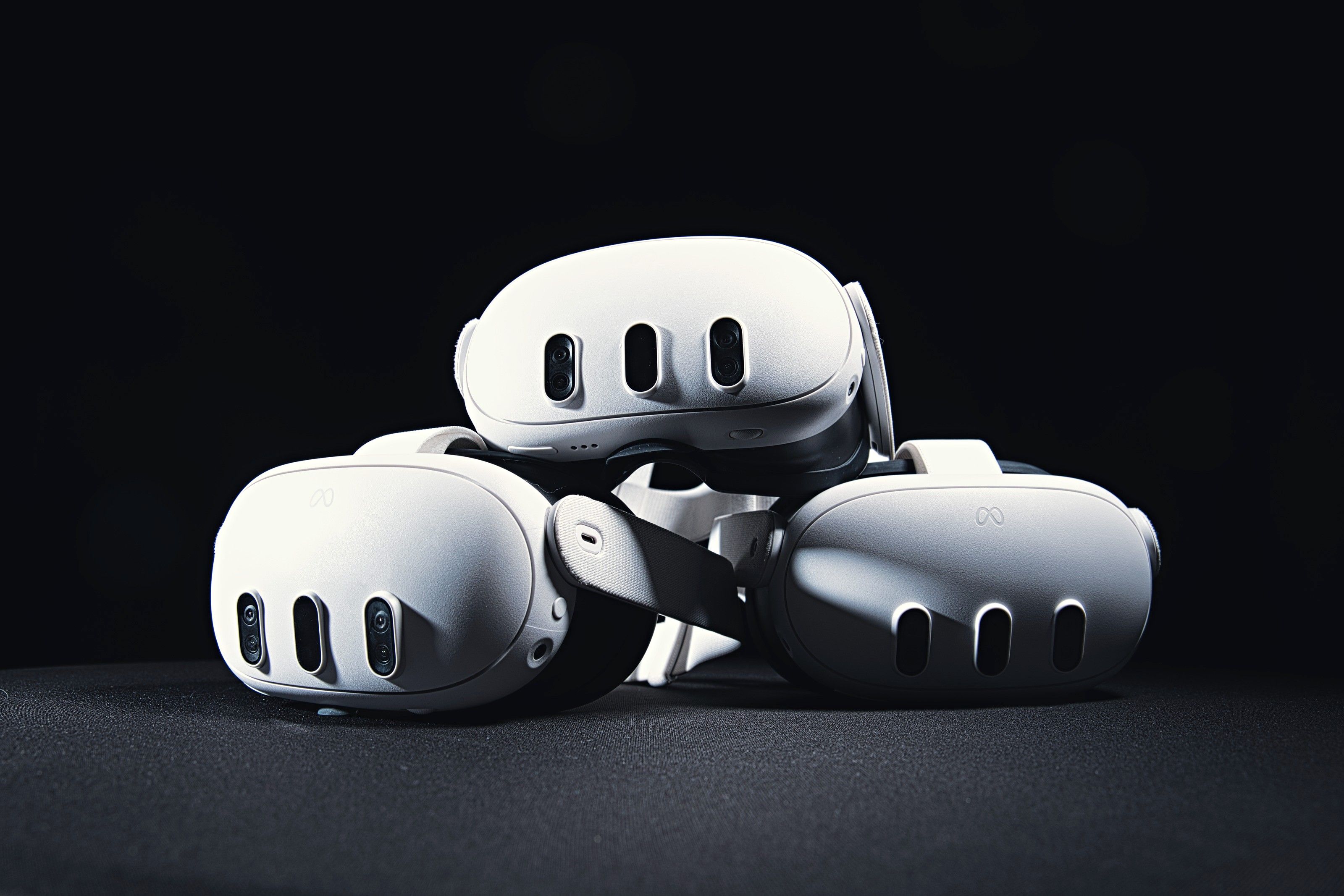 Three Meta Quest 3 headsets stacked on a dark table