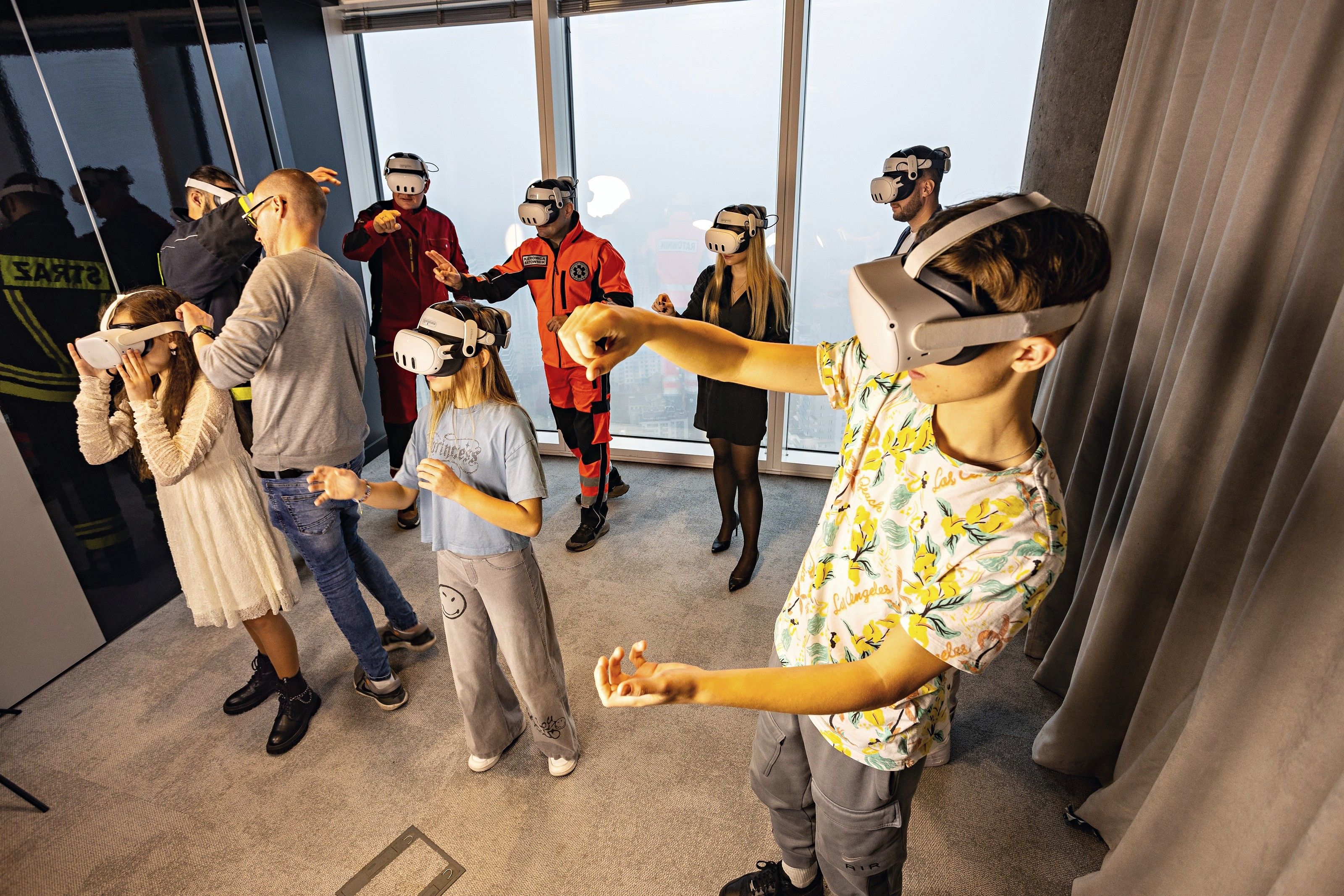Enfants et adultes essaient ensemble des scénarios de sécurité en VR, avec des pompiers et des secouristes en arrière-plan