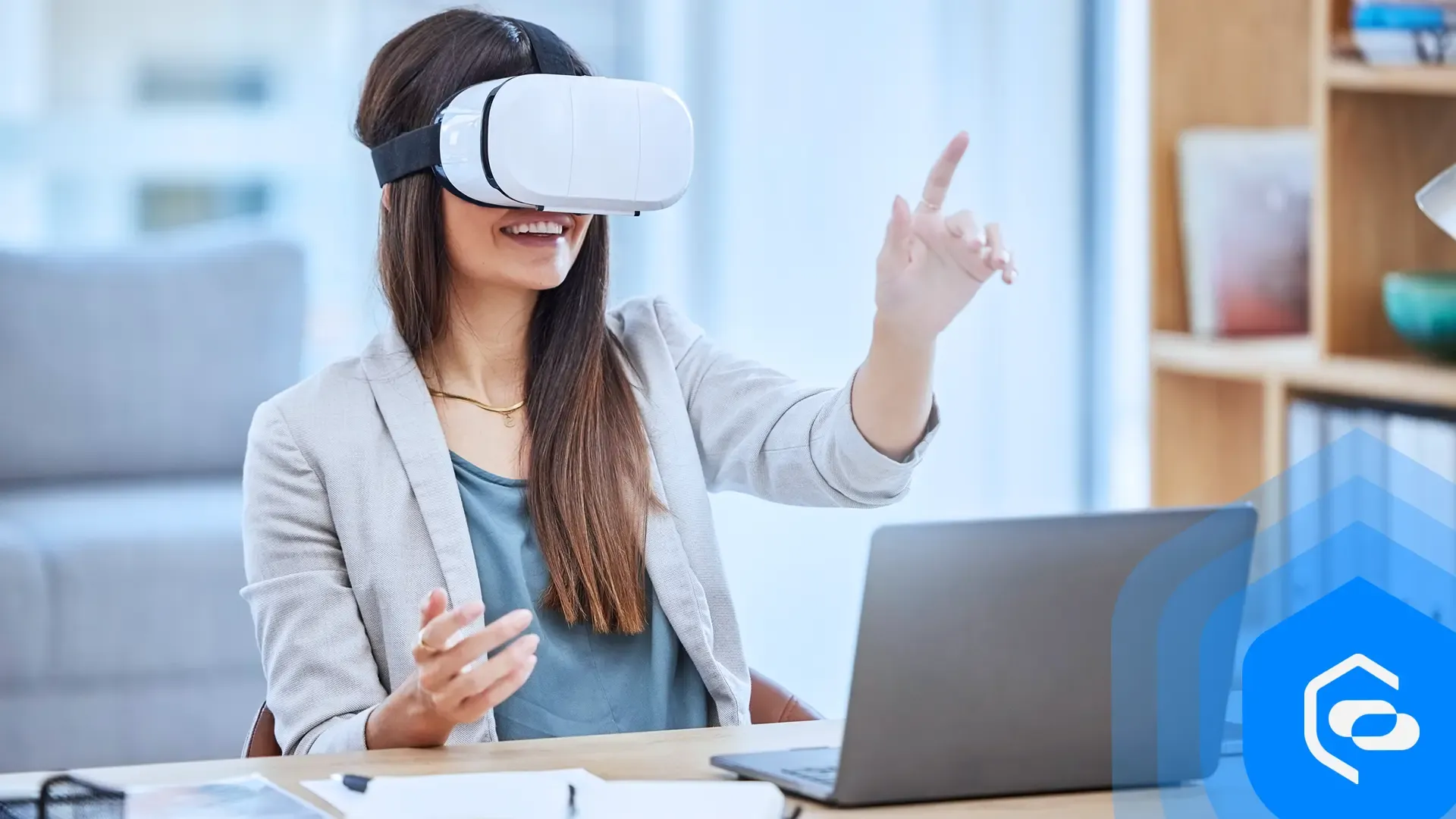 Une femme souriante portant un casque VR tend la main, assise à un bureau devant un ordinateur portable